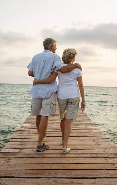 couple with their arms around each other while they walk down a dock by the ocean financial planner